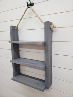 a shelf hanging on the side of a white building with rope attached to it and two shelves below