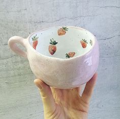 a hand holding a pink bowl with strawberries painted on the outside and inside it