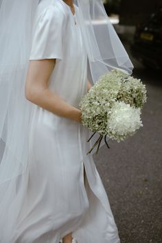 a woman in a white dress holding a bouquet of flowers and wearing a veil on her head