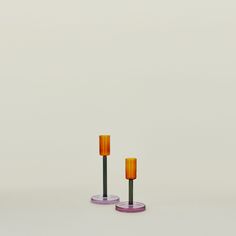 two orange and purple candles sitting next to each other on top of a white surface