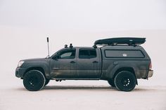 a truck with a surfboard on the roof is parked in the sand and it's snowing