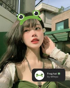 a woman with long hair wearing a green frog hat and holding her hand up to her ear