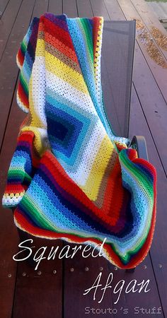 a multicolored crocheted blanket sitting on top of a wooden table next to a bench