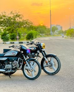 two motorcycles parked next to each other on the side of a road with trees in the background