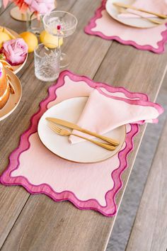 the table is set with pink and white placemats, goldware, and flowers