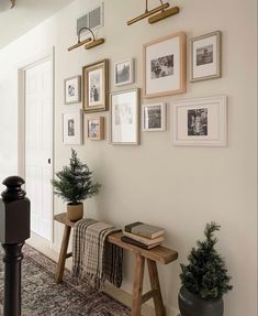 a hallway with pictures on the wall and a wooden bench in front of some potted plants