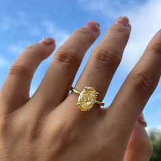 a woman's hand with a yellow diamond ring on her left hand and blue sky in the background