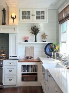 a kitchen with white cabinets and wood flooring next to a window filled with flowers