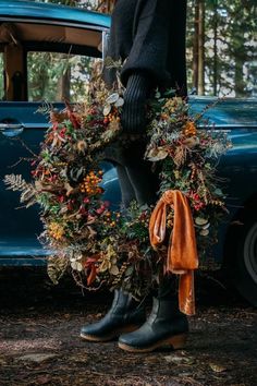 a person standing in front of an old blue car with a wreath on the door