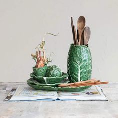 two green leafy vases with wooden spoons and utensils in them