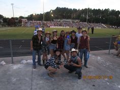 a group of people standing next to each other in front of a fence at a baseball field