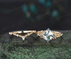 two gold rings with green and white stones on top of a stone slab in front of a black background