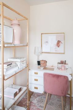 a pink chair sits in front of a white desk and shelving unit with gold trim