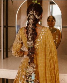 a woman with long hair in a yellow dress looking at her reflection in a mirror