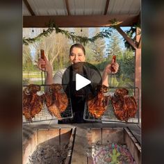 a woman holding two hot dogs in her hands while standing next to chicken on a rack