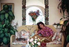 a woman sitting on top of a couch in a living room next to a potted plant