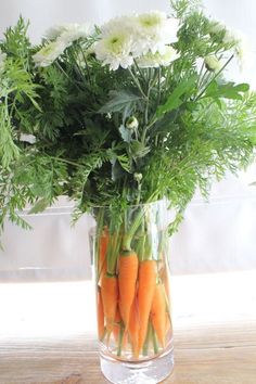 carrots are arranged in a glass vase with greenery and white flowers on the table