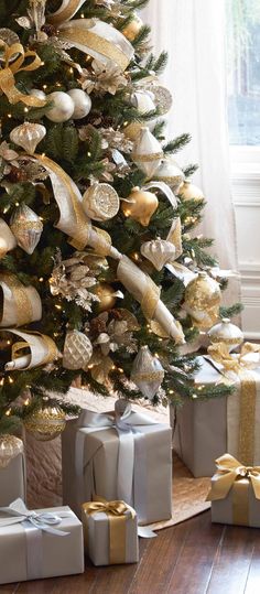 a christmas tree decorated with gold and silver ribbon, presents under the tree in front of a window