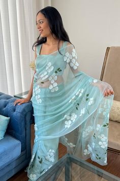 a woman standing in front of a couch wearing a blue dress with white flowers on it