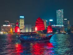 a boat with red sails is in the water near some tall buildings at night time