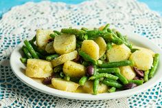 a white bowl filled with potatoes and green beans on top of a doily covered table