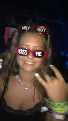 a woman wearing red glasses with the words kiss me written on them and two fingers in front of her face