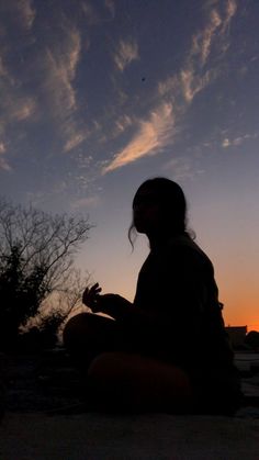 a woman sitting on the ground in front of a sunset