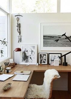 a desk with a chair and pictures on the wall next to it in front of a window