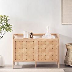 a living room with white walls and a wooden sideboard on top of a rug next to a potted plant