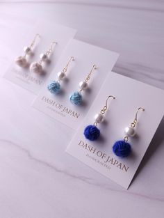 three pairs of dangle earrings with blue and white pom - poms hanging from them