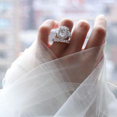 a woman's hand with a diamond ring on top of her wedding dress, in front of a window