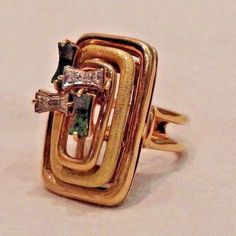 This uniquely designed modernist ring is one-of-a-kind! This is a large ring, rectangular in shape, that features 14K yellow gold, diamonds and green malachites The ring features three coils of 14K yellow gold that fit within each other with the middle coil having a snake-like texture detail The center, off to one side of the ring, features two curved pieces of green malachite as well as two sections that each feature two diamonds, with a total of four diamond chips The face of the ring measures Gold Multi-stone Rectangular Ring, Modernist Ring, Green Malachite, Large Ring, The Ring, Coils, The Middle, The Face, Jewelry Watches