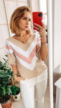 a woman taking a selfie while wearing white pants and a sweater with pink stripes