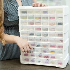 a woman is holding a large plastic storage box with many different colored tapes in it