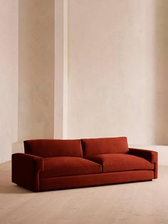 a red couch sitting on top of a hard wood floor next to a white wall