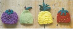 three crocheted strawberries are lined up on a wooden surface, one is red, one is green and the other is yellow