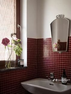 a white sink sitting under a bathroom mirror next to a vase with flowers in it