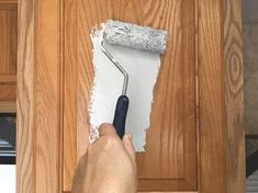 a person holding a paint roller in front of a kitchen cabinet with white paint on it