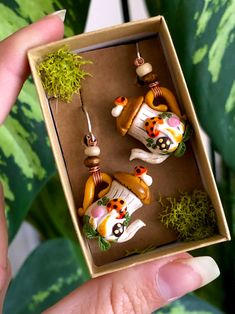 a person is holding two small ornaments in a box that are decorated with animals and plants