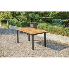 a wooden table sitting in the middle of a gravel covered area next to bushes and trees