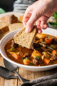 a person dipping bread into a bowl of stew