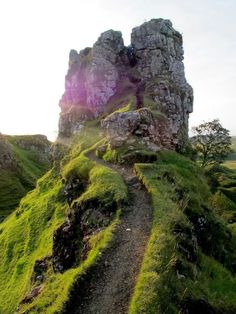 an old stone castle with grass growing on the side and dirt path leading up to it