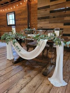 the table is decorated with greenery, candles and white draping on it