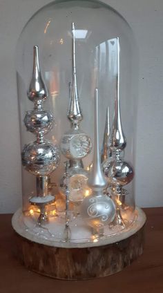 a glass dome with silver and white ornaments inside it on a wooden table next to a wall