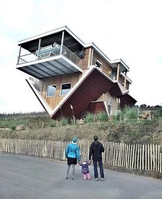 two people and a child are standing in front of an upside down house