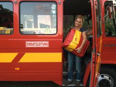 a woman standing in the doorway of a red and yellow bus with her shopping bags