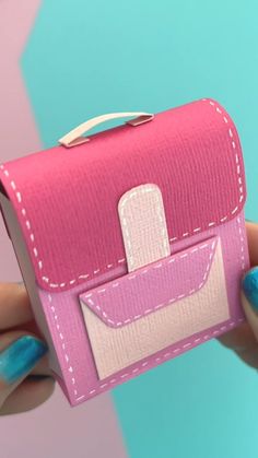 a hand holding a pink and white purse with blue nail polishes on the nails