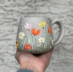 a hand holding a coffee cup with flowers painted on it