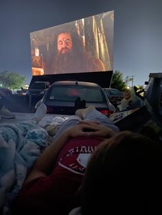 people laying in bed watching a movie on the big screen at night with cars passing by