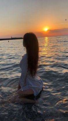 a woman sitting in the water at sunset